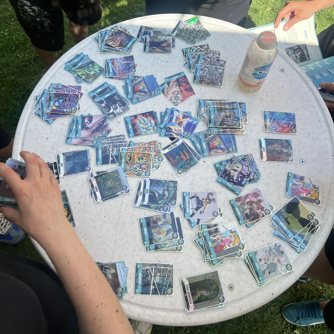Des festivaliers remplissent des albums bleus avec des stickers à collectionner de street art étalés sur une table ronde
