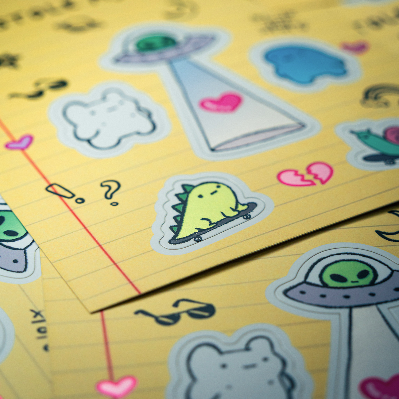 Stickers on lined paper feature cute dinos, UFOs, and hearts, including a green dinosaur and broken heart symbol, in pastel colors.