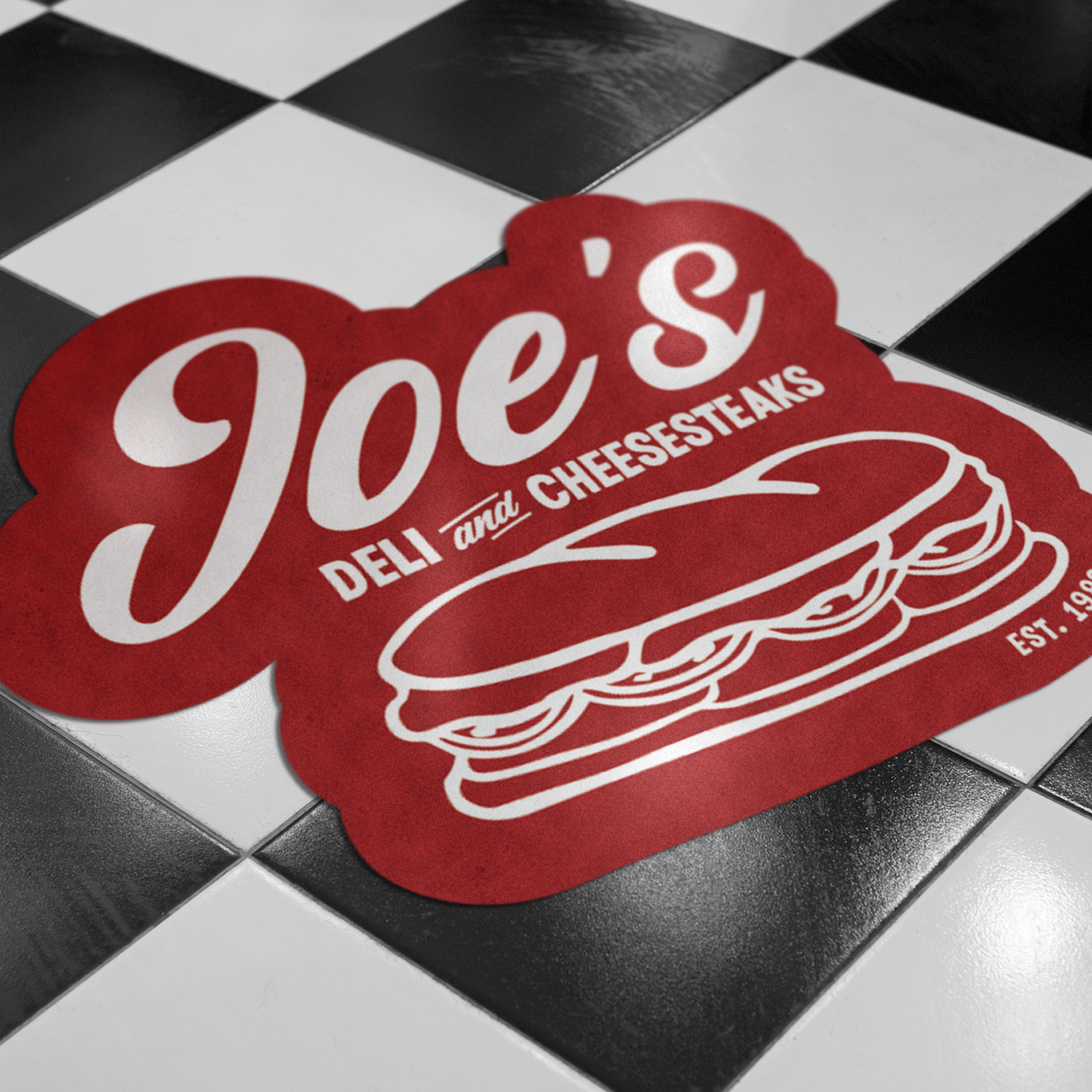 Décalcomanie de sol personnalisée avec le logo rouge Joe's Deli and Cheesesteaks sur un carrelage en damier noir et blanc