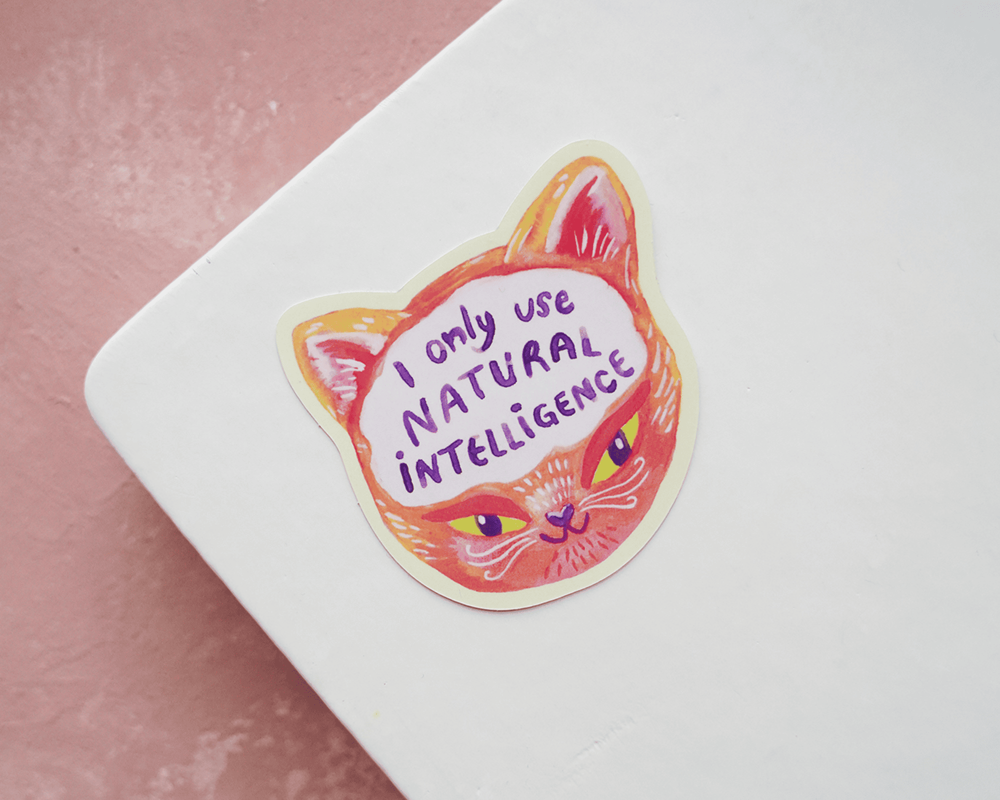 Sticker à la forme tête de chat avec le texte "I only use natural intelligence" sur un carnet blanc